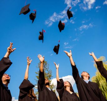 Congratulations! Low angle view of happy group of six young cheerful multi ethnic graduates in black gowns are throwing up their hats in the air and celebrating, laughing, enjoying